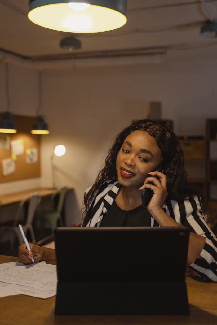 about-04 Confident businesswoman multitasking on phone and laptop in a warm office atmosphere.